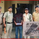 उत्तराखंड एसटीएफ द्वारा आतंकी लिंक में गिरफ्तार युवक, पृष्ठभूमि में पुलिस और देहरादून शहर