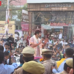 वाराणसी में पंडित धीरेंद्र कृष्ण शास्त्री का रथयात्रा में भक्तों का अभिवादन करते हुए