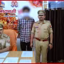 एक पुलिस अधिकारी गिरफ्तार आरोपी के साथ, हाथ में मोबाइल फोन।