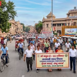 वाराणसी में लोग हाथों में बैनर लेकर पैदल चलते हुए, उनके पीछे साइकिल और इलेक्ट्रिक वाहन