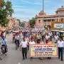 वाराणसी में लोग हाथों में बैनर लेकर पैदल चलते हुए, उनके पीछे साइकिल और इलेक्ट्रिक वाहन