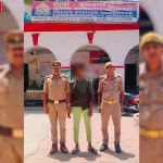 रामनगर पुलिस अधिकारी, एक अपराधी को हथकड़ी लगाए हुए, पीछे पुलिस स्टेशन का दृश्य