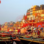 वाराणसी के गंगा घाट पर कतार में खड़ी नावें, कुछ नावों पर यात्री बैठे हैं और पास में गंगा नदी बह रही है।