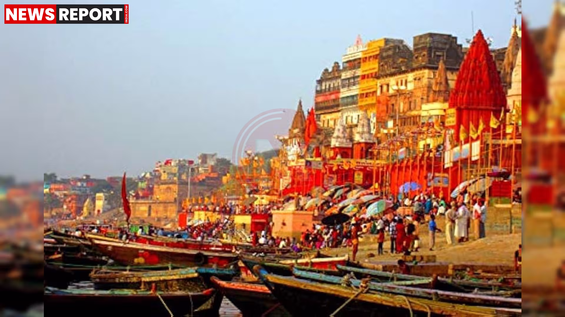 वाराणसी के गंगा घाट पर कतार में खड़ी नावें, कुछ नावों पर यात्री बैठे हैं और पास में गंगा नदी बह रही है।