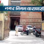 बारिश में जलभराव के दौरान एक खुले मैनहोल के पास चेतावनी बोर्ड और आसपास लोग।