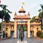 काशी हिंदू विश्वविद्यालय (BHU) का मुख्य द्वार और उस पर निलंबन आदेश की प्रतिलिपि पकड़े एक छात्र की सांकेतिक तस्वीर।