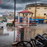 बारिश और तेज हवाओं के बीच वाराणसी में लोग छाता लिए चलते हुए